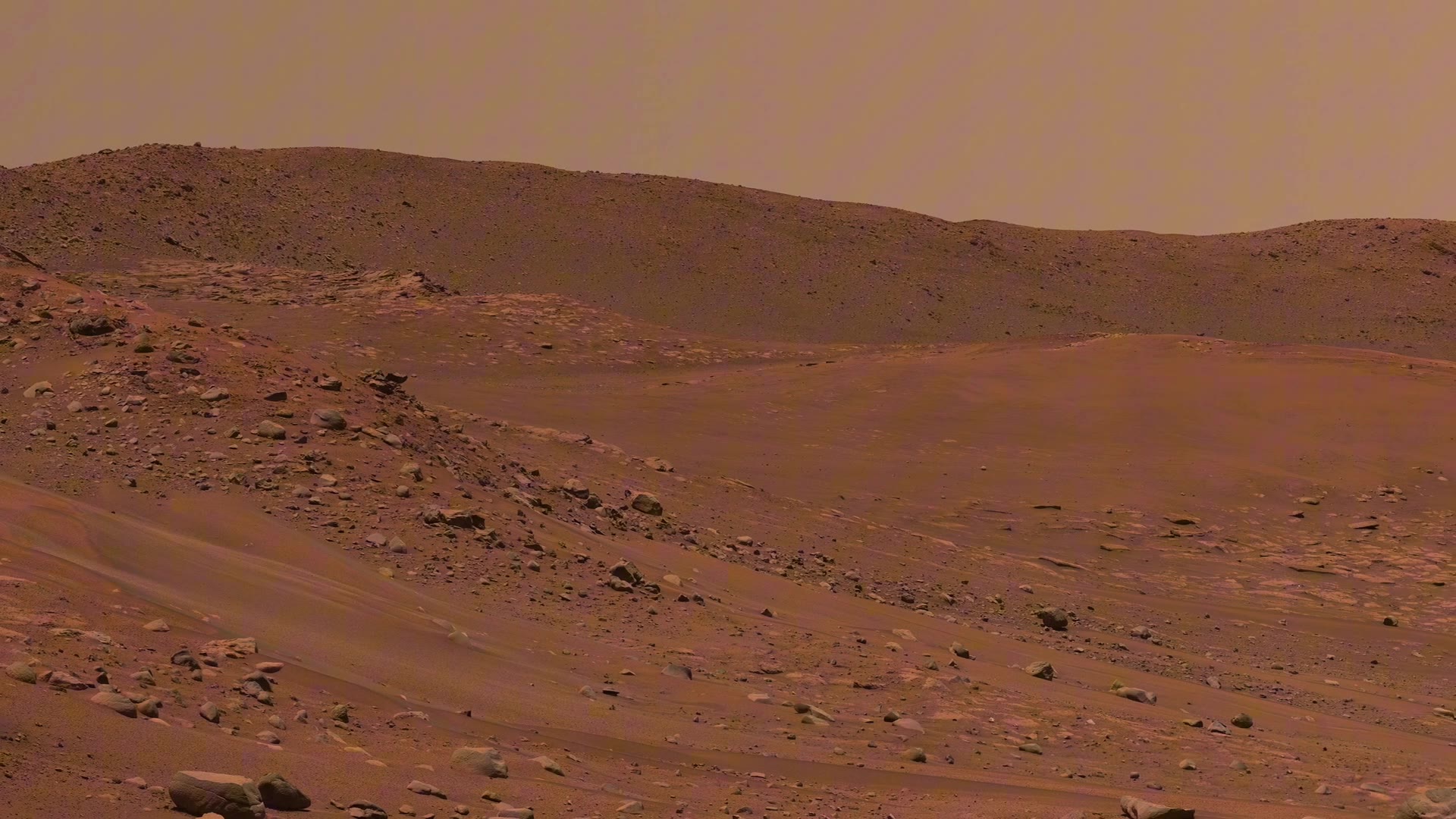 Rover-height pan across rust hills and a dust-hazed Martian valley, pale sky over a rock-strewn slope.